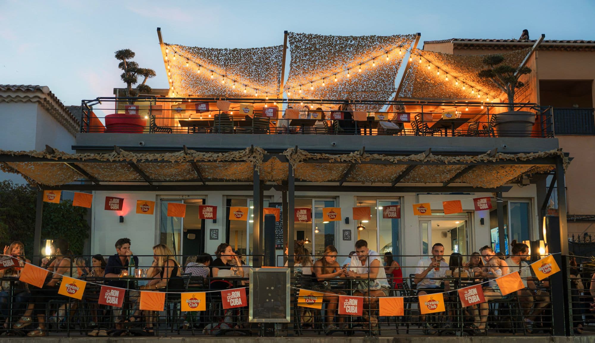 La façade du Café du Port en soirée, la terrasse et le rooftop illuminés